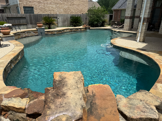 Freeform in-ground pool with a rock waterfall, filter and pump running clear